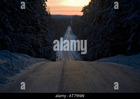 Scena di un vuoto, icy country road attraverso la foresta in inverno a sera Finlandia Foto Stock