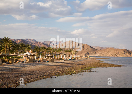 Vista lungo la spiaggia sabbiosa di aspre colline sulla costa del Mar Rosso con la gente a prendere il sole nel tardo pomeriggio di sole Taba Heights Egitto Foto Stock