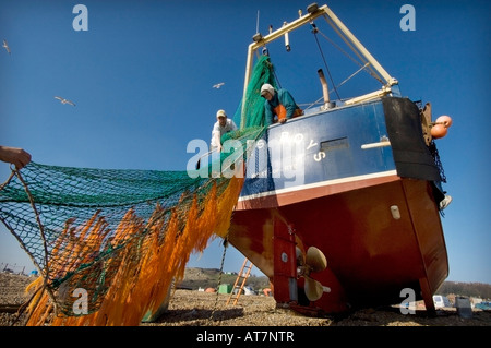 Due equipaggi dalla piccola barca da pesca Roys Boys controllare le reti da pesca dopo essere stato winched up Hastings beach Foto Stock