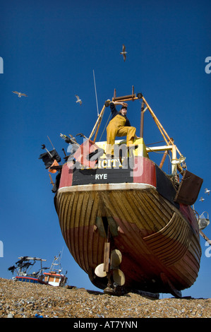 Un crewman in incerato su un piccolo legno barca da pesca a terra sulla spiaggia di Hastings Sussex Foto Stock