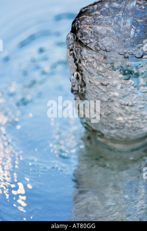 Versare acqua in un bicchiere che si erge su uno specchio che riflette il cielo blu Foto Stock