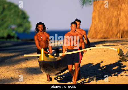 3 giovani uomini ottenere pronto per l'allenamento nel loro canoe outrigger nell'oceano blu acque al largo della Big Island delle Hawaii Foto Stock