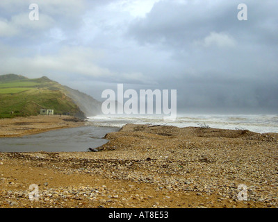 Giorno tempestoso con grandi onde e spruzzare la rottura a Charmouth sulla costa Dorest un piccolo estuario del fiume scorre in mare attraverso una pietra di ghiaia e di sabbia spiaggia Foto Stock