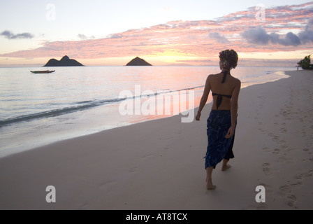 Un alto giovane donna cammina lungo la splendida spiaggia di Lanikai Beach all'alba con le isole Mokulua nella distanza. Foto Stock