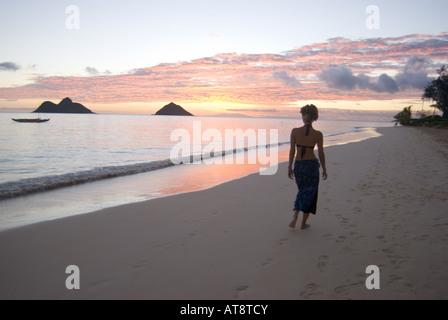 Un alto giovane donna cammina lungo la splendida spiaggia di Lanikai Beach all'alba con le isole Mokulua nella distanza. Foto Stock