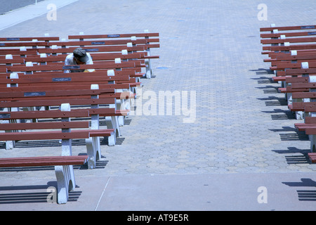 Passerella piastrellato con due righe di cemento vuote panche di legno con corridoio in centro. Uomo solitario con la testa rivolta verso il basso sulla destra. Foto Stock