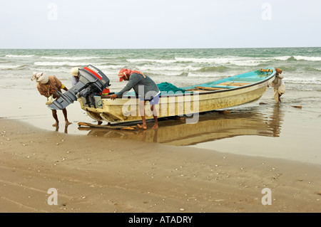 I pescatori spingendo le piccole barche da pesca fino al Sawadi beach l'utilizzo di registri a rotolare su Oman Foto Stock