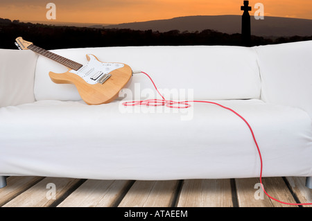 In legno stile stratocaster chitarra elettrica sdraiata su un lettino bianco davanti al tramonto sulla scena tavoloni Foto Stock