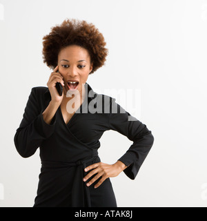 Donna che parla su cellulare guardando scioccato contro uno sfondo bianco Foto Stock