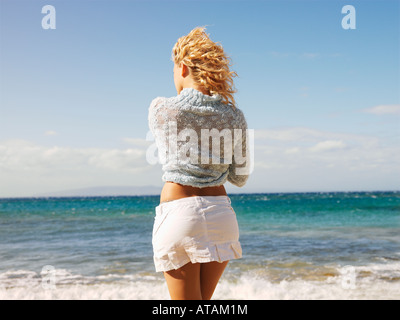 Vista posteriore della giovane donna bionda che sta in piedi in acqua s edge a Maui Hawaii spiaggia ammirate l'oceano Foto Stock