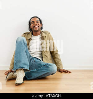 Uomo seduto sul pavimento di legno di casa sorridente Foto Stock