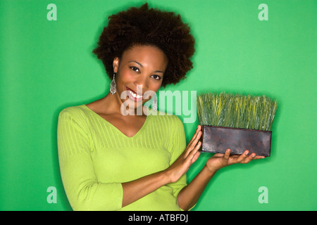 Donna sorridente con afro holding pot di erba contro lo sfondo di colore verde Foto Stock
