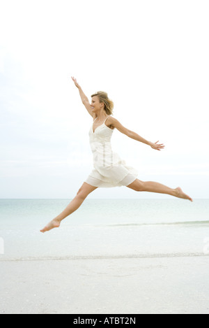 Giovane donna in sundress saltare in aria, ocean horizon in background, braccia, vista laterale Foto Stock