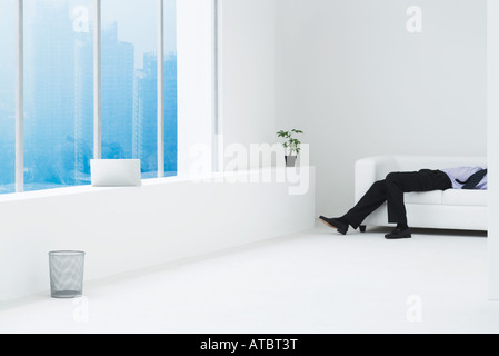 Uomo d'affari sdraiato sul divano minimalista in alto appartamento vista ritagliata Foto Stock