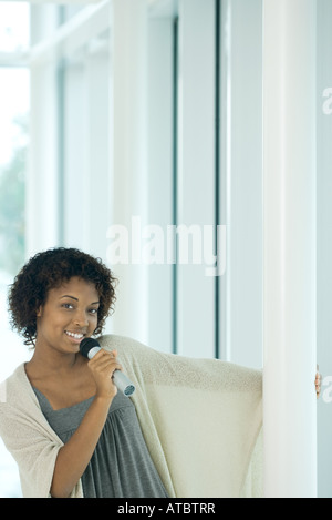 Giovane donna di tenere su palo, cantando nel microfono, sorridente in telecamera Foto Stock