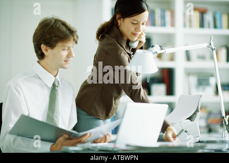 Maschio e femmina dei colleghi al desk, un uomo guarda il computer portatile, donna usando il telefono Foto Stock