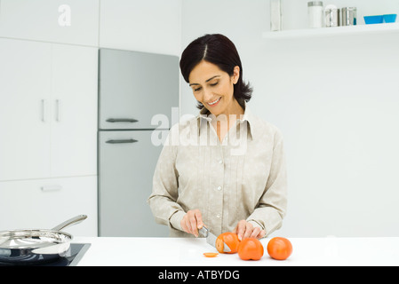 Donna in piedi al bancone cucina, Affettare i pomodori con il coltello Foto Stock