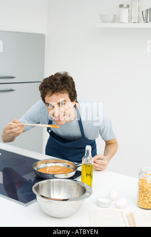 L'uomo la cottura in cucina, la piegatura oltre alla salsa il sapore, sorridente in telecamera Foto Stock
