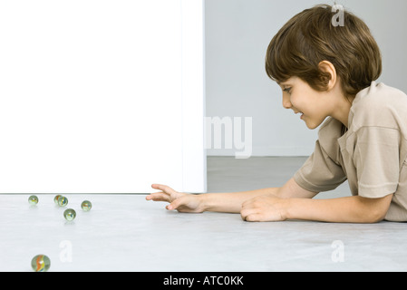 Little Boy giacente a terra giocando con marmi, vista laterale Foto Stock