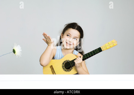 Piccola ragazza con chitarra, mano alzata nel gesto sorridente Foto Stock