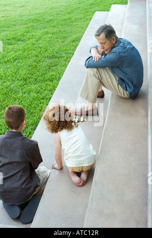 Nonno e due nipoti giocare con automobili giocattolo insieme su scale, ad alto angolo di visione Foto Stock