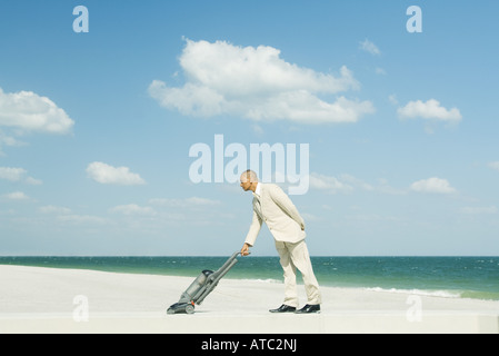 Uomo in tuta con aspirapolvere sulla spiaggia a piena lunghezza Foto Stock