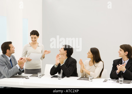 Imprenditrice e permanente parlando, i colleghi seduti battimani, sorridente Foto Stock