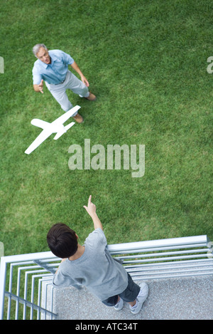 Ragazzo in piedi sul balcone, gettando aeroplano giocattolo al nonno in piedi al di sotto, ad alto angolo di visione Foto Stock