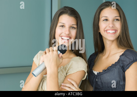 Teenage gemelle affiancate, entrambe sorridenti, uno tenendo il microfono Foto Stock