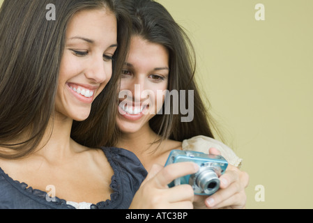 Teenage gemelle guardando la fotocamera digitale insieme, sia sorridente Foto Stock