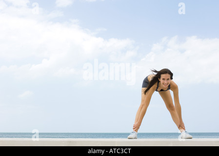 Giovane donna di piegarsi, toccando le caviglie, sorridente in telecamera Foto Stock