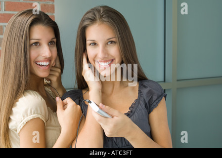 Teenage gemelle ascoltando mp3 player insieme, sia sorridente, uno che guarda in telecamera Foto Stock