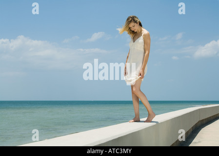 Giovane donna in sundress permanente sulla bassa parete accanto al mare, gli occhi chiusi Foto Stock