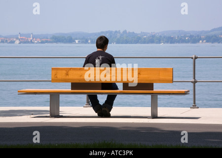 Uomo si siede su una banca presso la banca di un lago Foto Stock