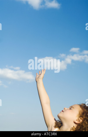 Bambina raggiungendo una mano verso il cielo, capo indietro a occhi chiusi, vista ritagliata Foto Stock