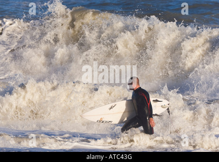 Lone surfer con scheda sulla riva del mare di entrare surf Foto Stock