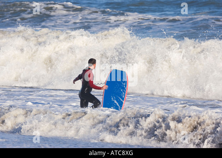 Lone surfer con scheda sulla riva del mare di entrare surf Foto Stock