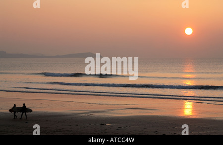 Due surfisti di camminare sulla spiaggia con un tramonto dorato Foto Stock