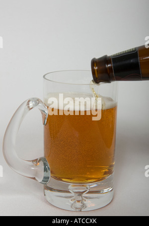 Boccale di birra con birra ambrata versata da una bottiglia su bianco senza saldatura Foto Stock