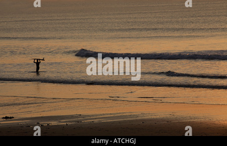 Un singolo lone surfer wades fuori verso le onde portando la sua scheda sulla sua testa Foto Stock