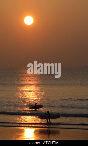 Due surfisti sulla spiaggia stagliano da sole di setting Foto Stock