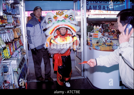 Un leone entra in uno stabilimento per essere alimentata con una busta rossa contenente denaro dal proprietario del negozio, annuale danze lion,Chinatown, NYC Foto Stock