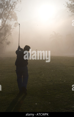 La mattina presto i golfisti stagliano in una fitta nebbia con un Rising Sun Foto Stock