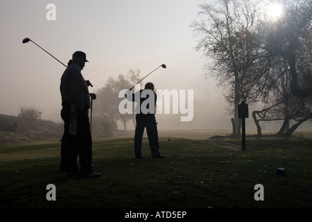 La mattina presto i golfisti stagliano in una fitta nebbia con un Rising Sun Foto Stock