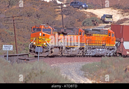 Tre locomotive BNSF numeri 4302 1038 e 5457 con un treno di container di spedizione sulla salita del Cajon Pass Foto Stock