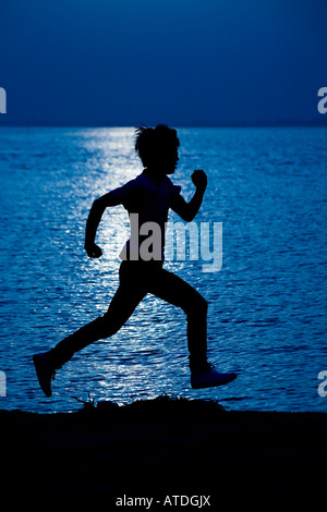 Silhouette di un giovane uomo che corre dal lago Foto Stock