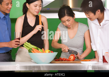 Giovane donna il taglio di vegetali con i suoi tre amici in piedi accanto a lei Foto Stock