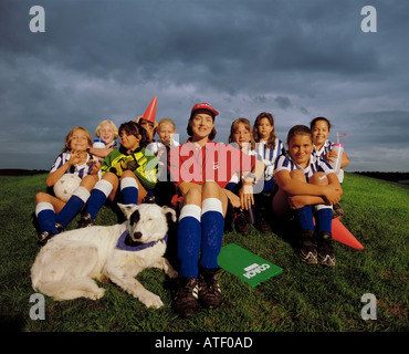 Adulti femmine allenatore di calcio seduto sul campo circondato da giovani ragazze del team con a squadra mascotte cane Foto Stock