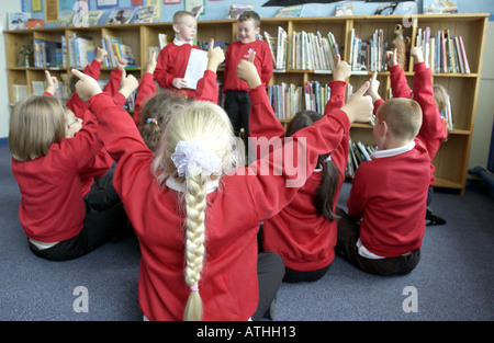 Desiderosi di bambini con le braccia in aria in una scuola primaria classroom Foto Stock