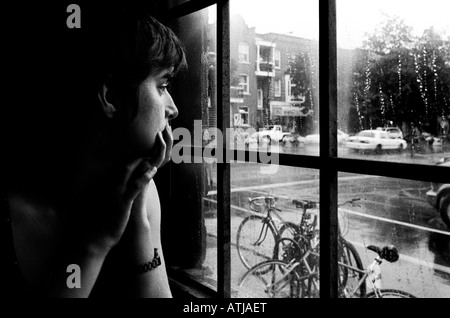 Capelli corti donna giovane con mento in mani guarda fuori finestra sulla città piovosa street. Foto Stock